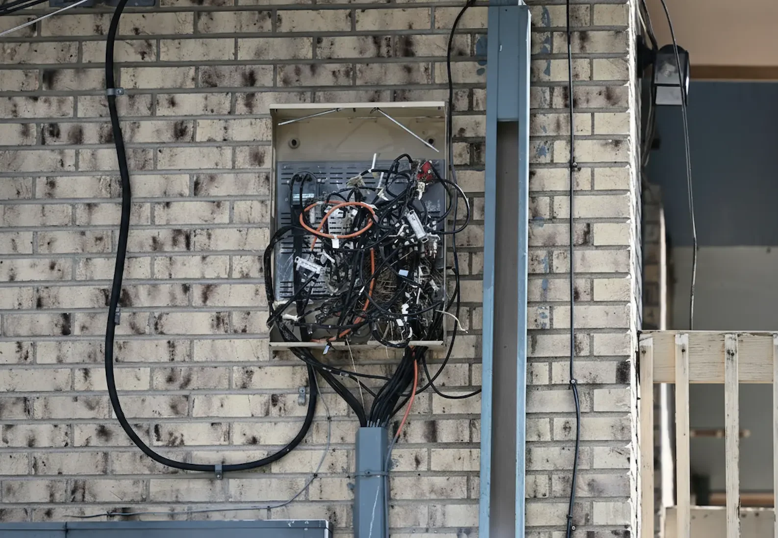 A chaotic and tangled mess of black and orange electrical wires inside an open, weathered exterior junction box on a brick wall.