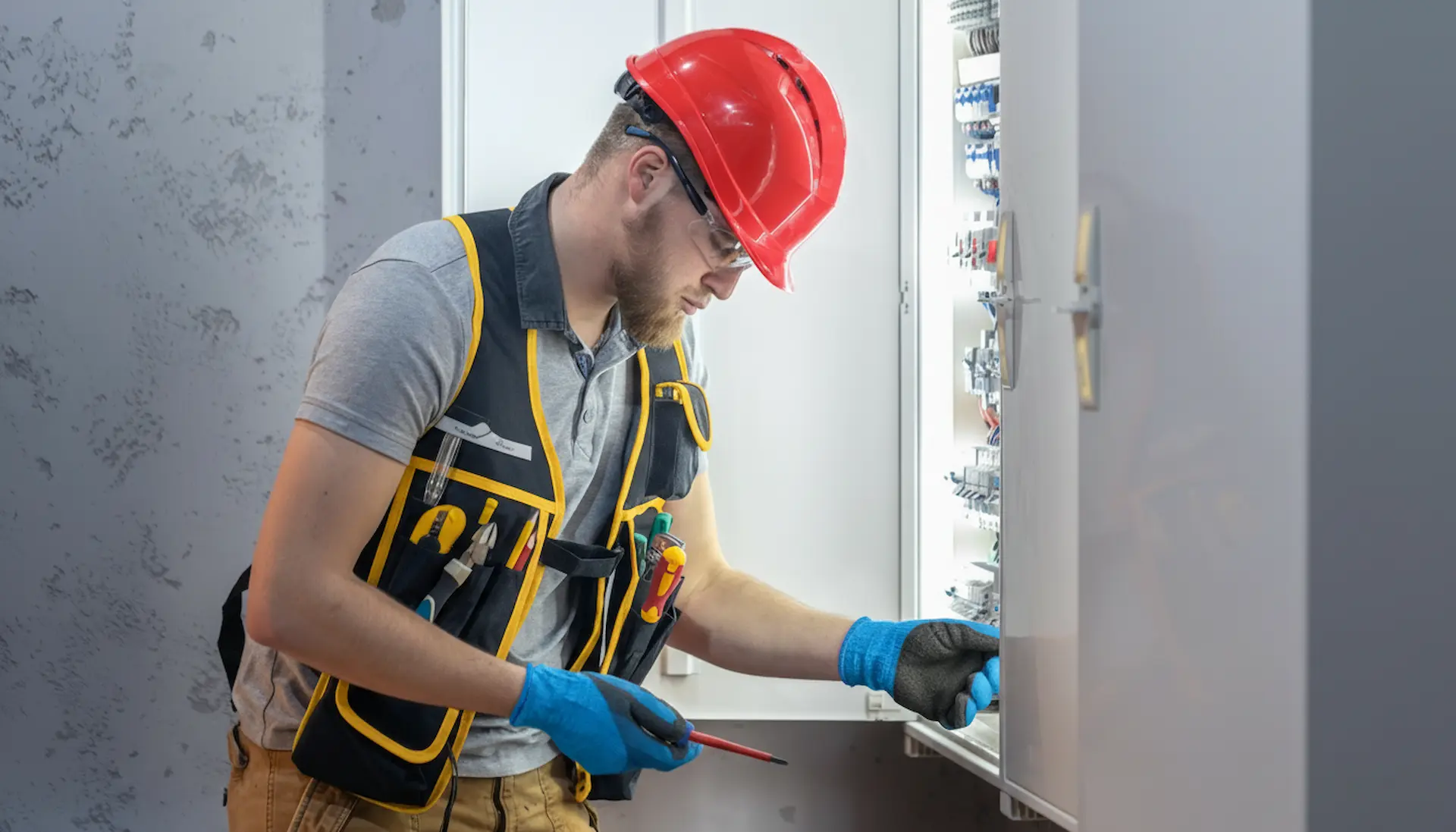 A licensed same-day emergency electrician wearing protective gear, including a hard hat and safety gloves, performing an essential electrical repair on a residential breaker panel to resolve power outages and safety hazards.