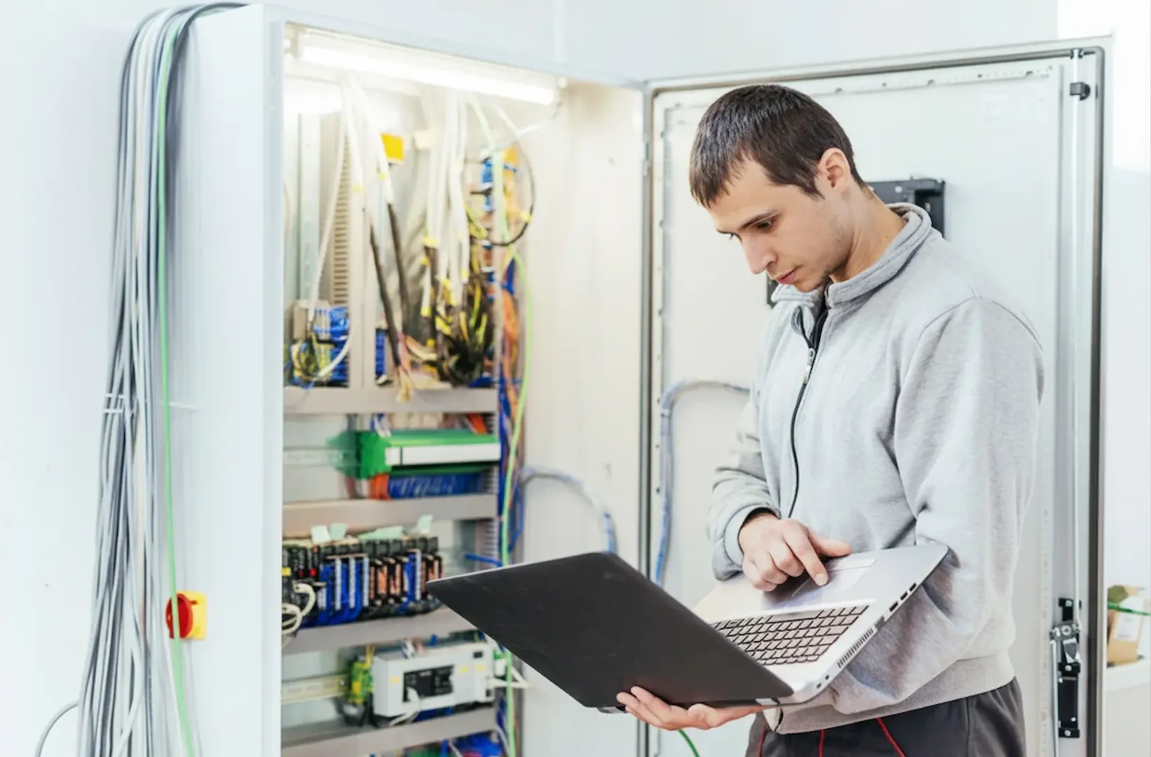 A technician using a laptop computer to configure and test complex wiring during a high-tech industrial electrical panel upgrade.