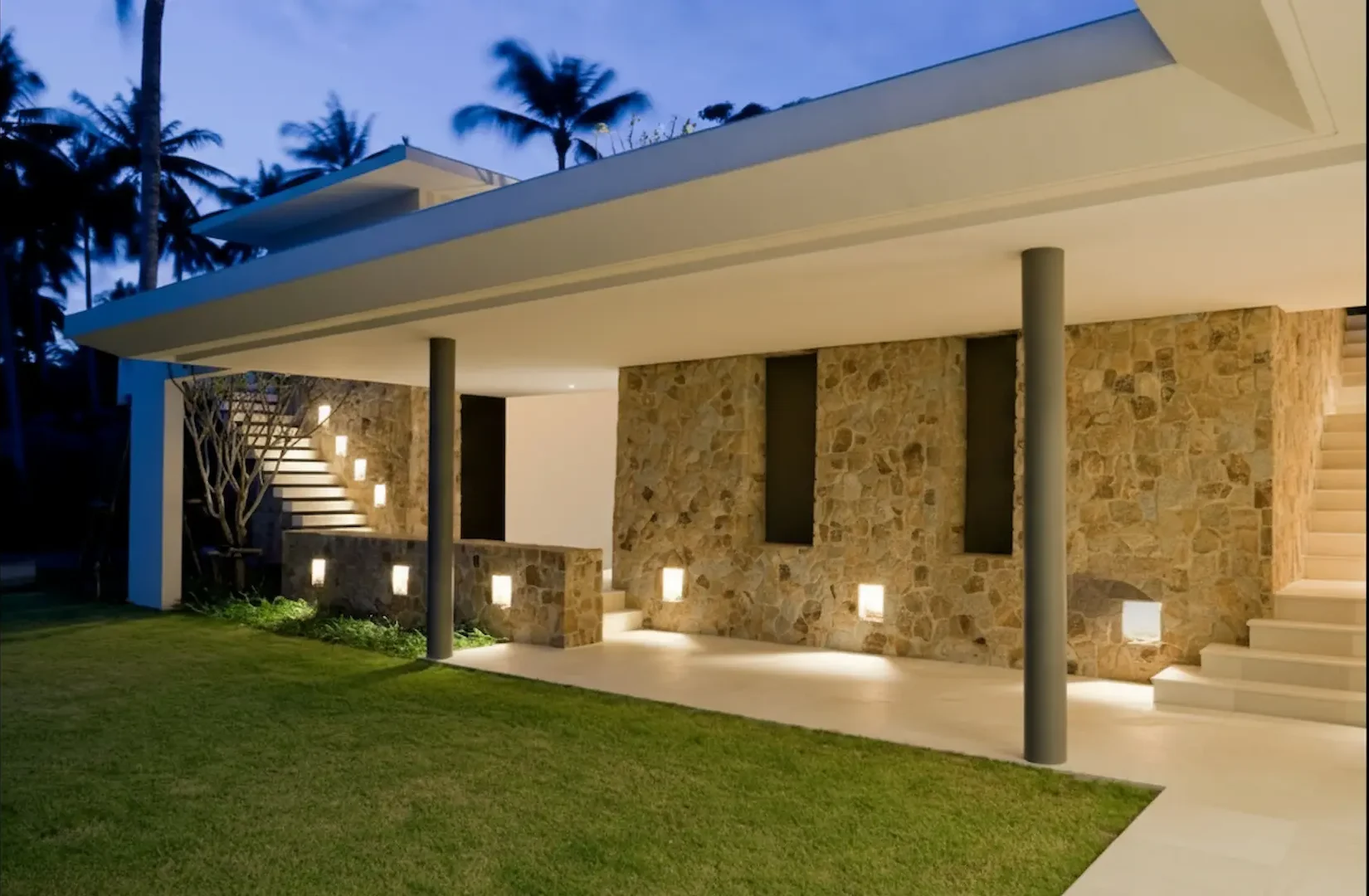 Outdoor Lighting Design: Exterior view of a stone-clad home featuring square recessed wall lights and illuminated stairs leading to a modern terrace.