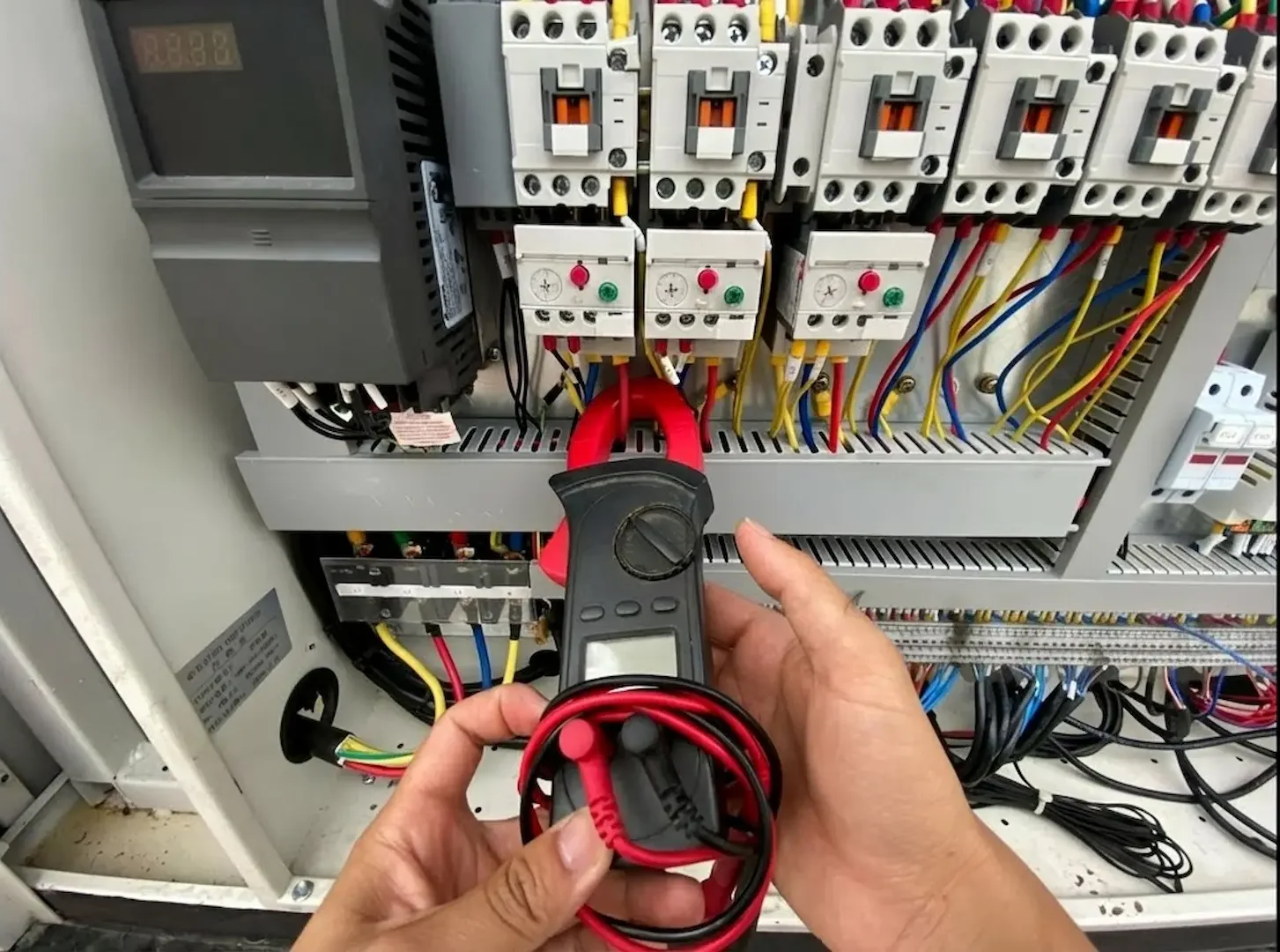 Close-up of a electrician using a digital clamp multimeter to test voltage and circuit load in a service panel.
