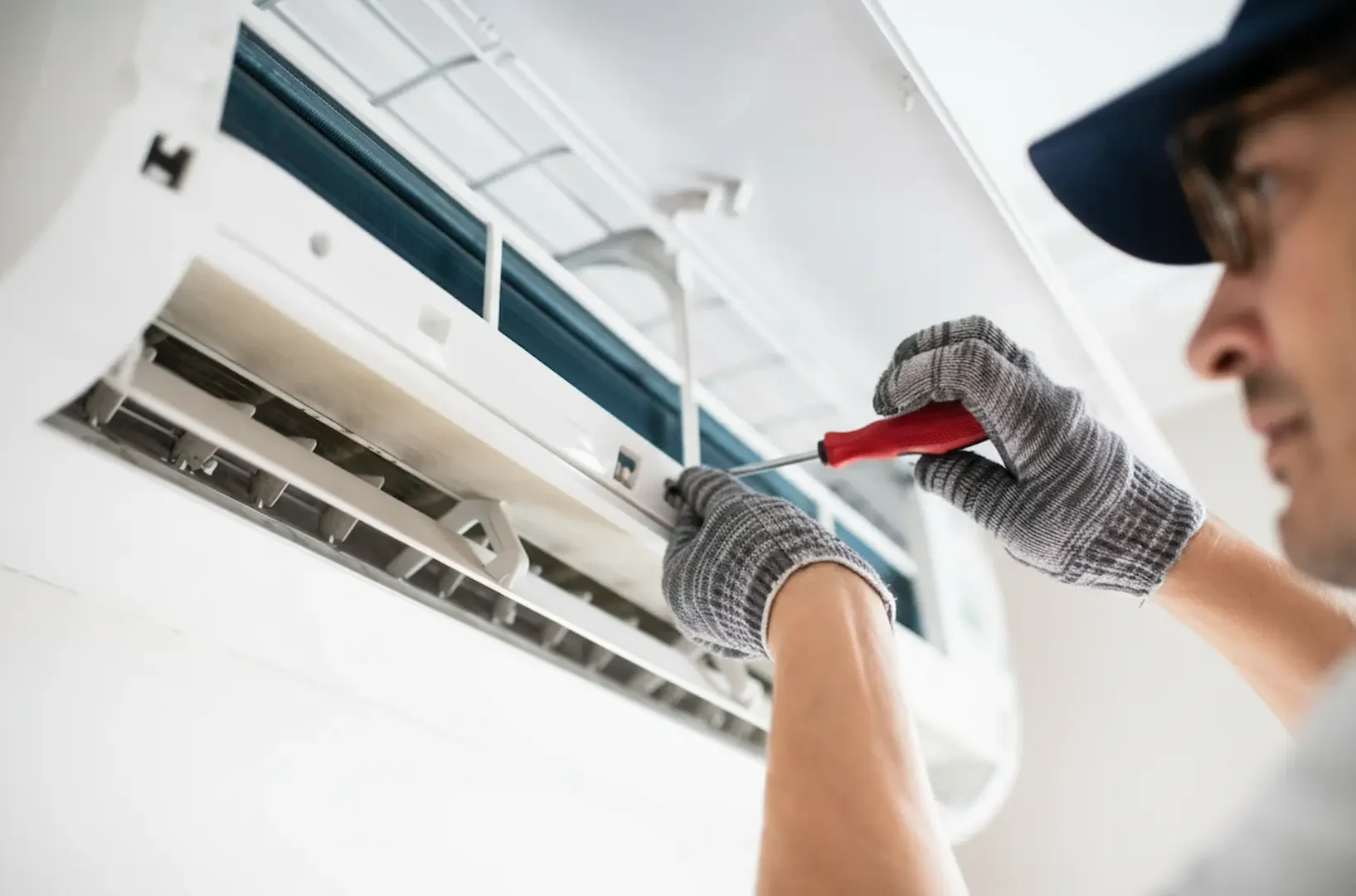 Emergency Electrical Service: Professional technician in gloves using a screwdriver to complete the electrical connections for a wall-mounted mini-split air conditioning unit
