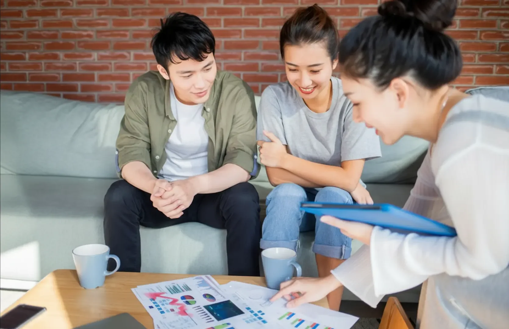 Booking an Electrical Repair: A professional consultant in a white shirt presenting data visualizations and financial charts on a coffee table to a young couple sitting on a couch.