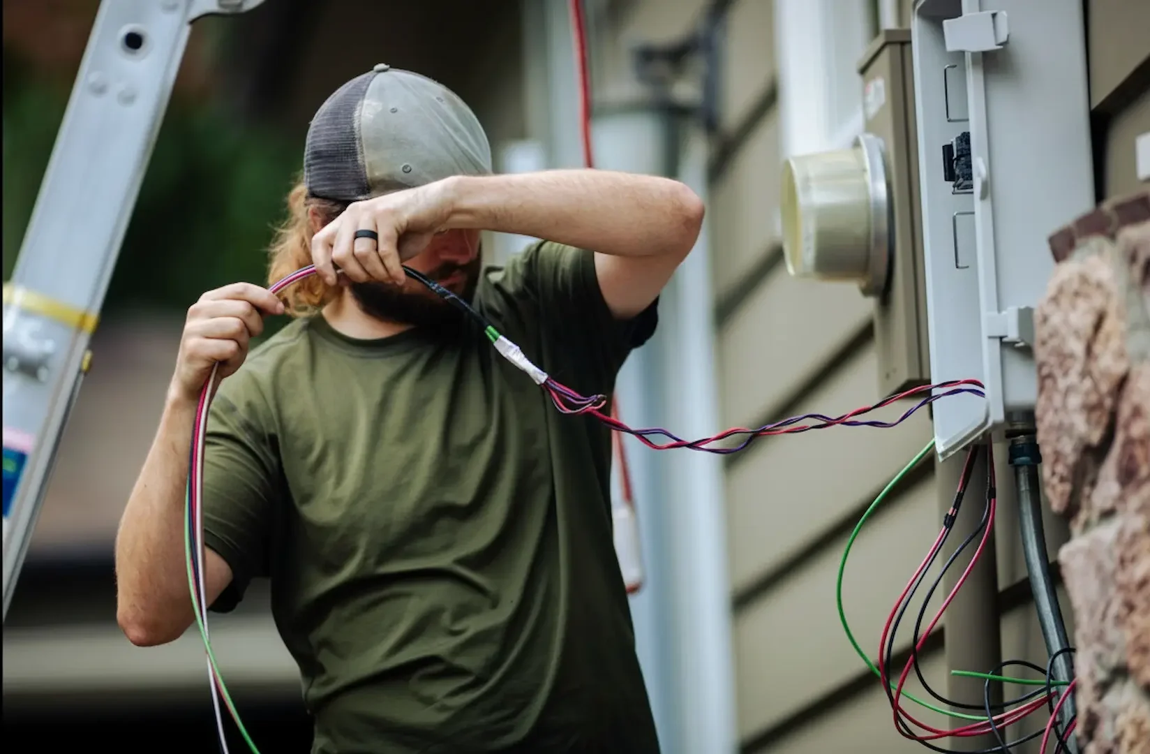 Panel replacement: A licensed electrician pulling main service wires into an outdoor electrical panel on a residential home exterior.