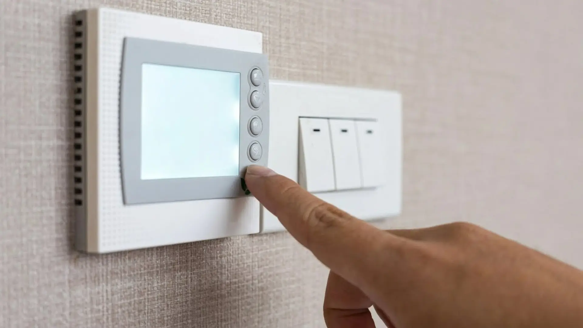 Panel upgrade cost: A homeowner adjusting settings on a wall-mounted smart home digital control interface next to modern light switches.