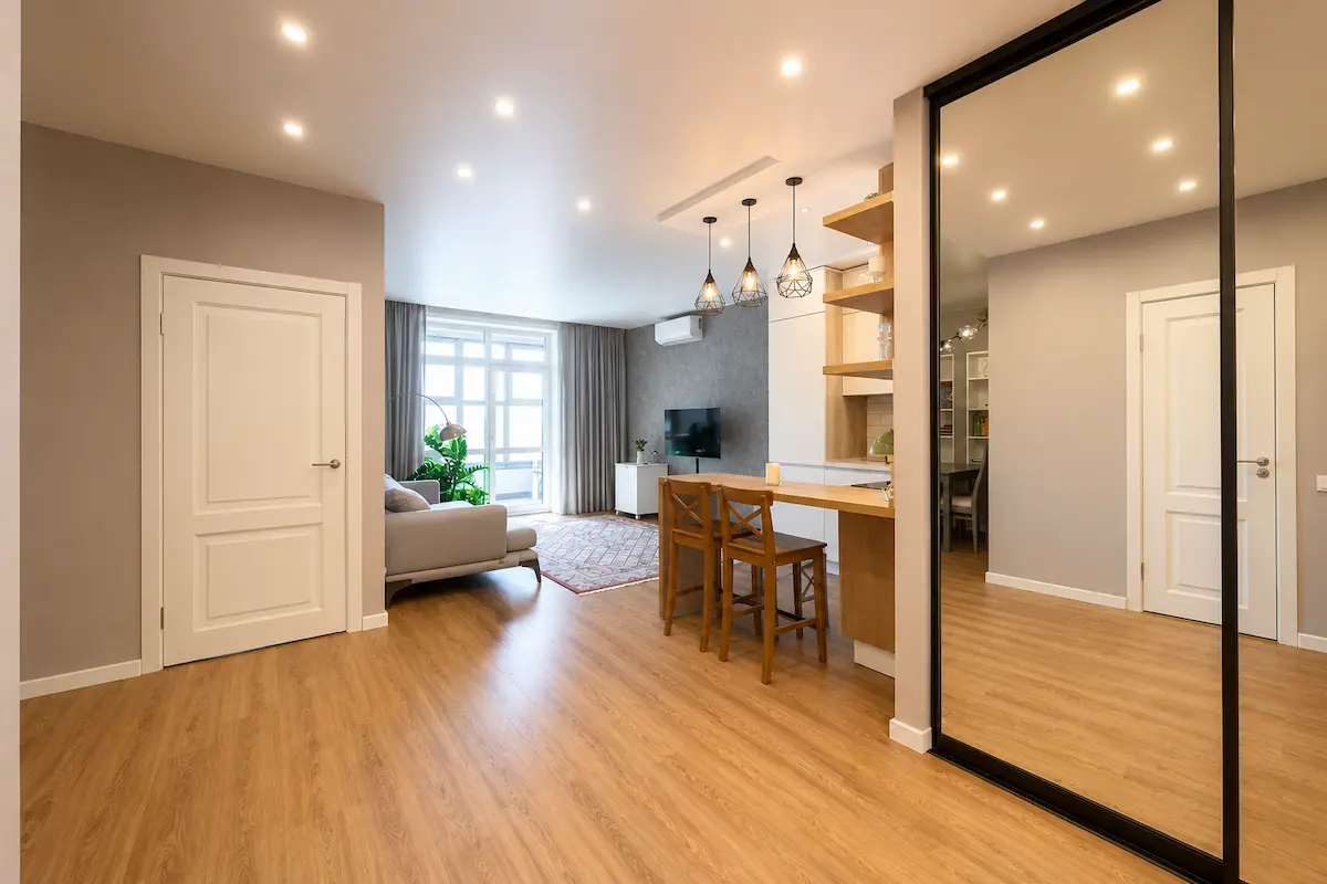 Recessed lighting installed throughout a modern open-concept apartment featuring a living room, kitchen island, wood flooring, and bright ambient illumination.